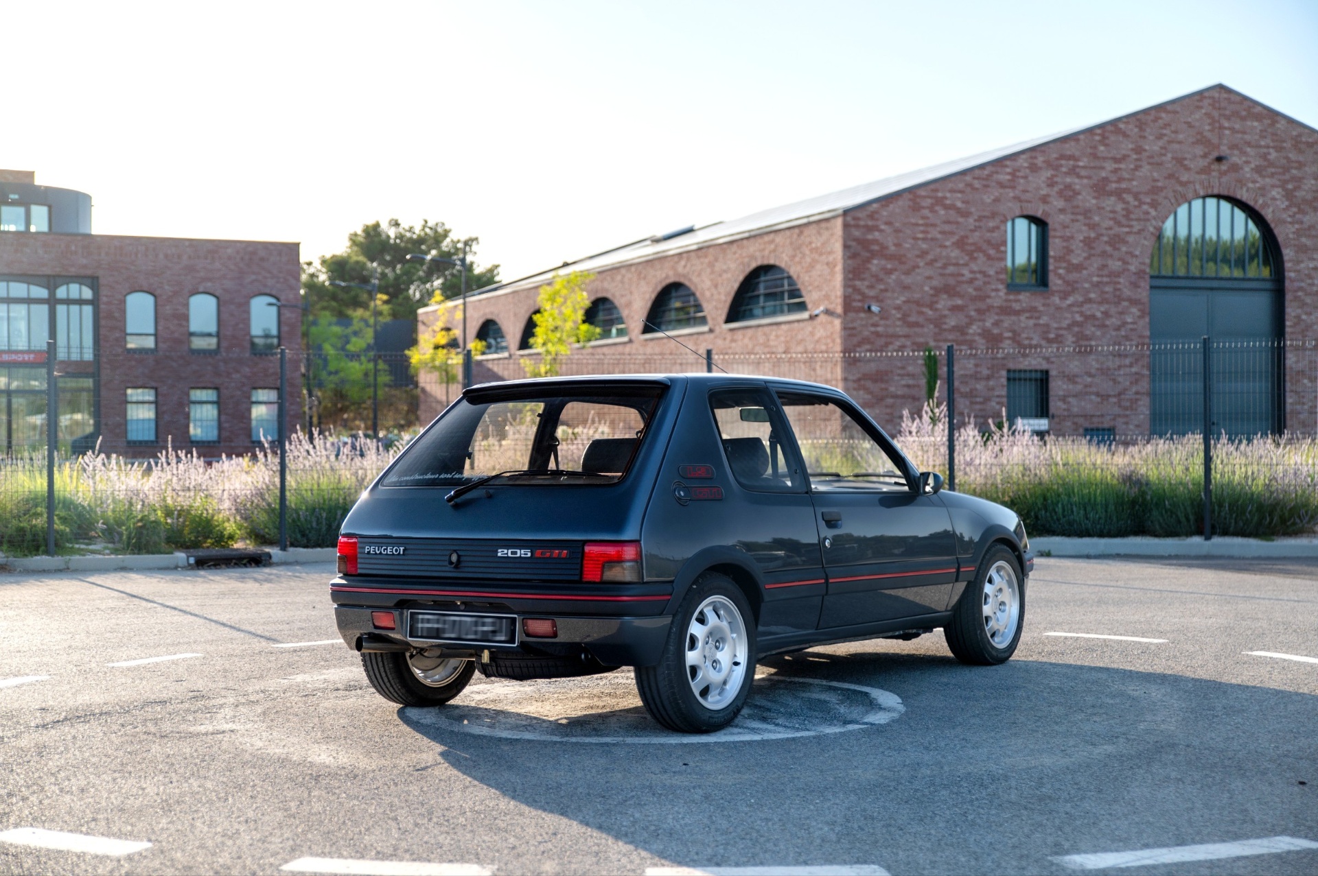 Peugeot 205 GTI 1.9 vue arrière trois quarts gris graphite devant bâtiment en briques