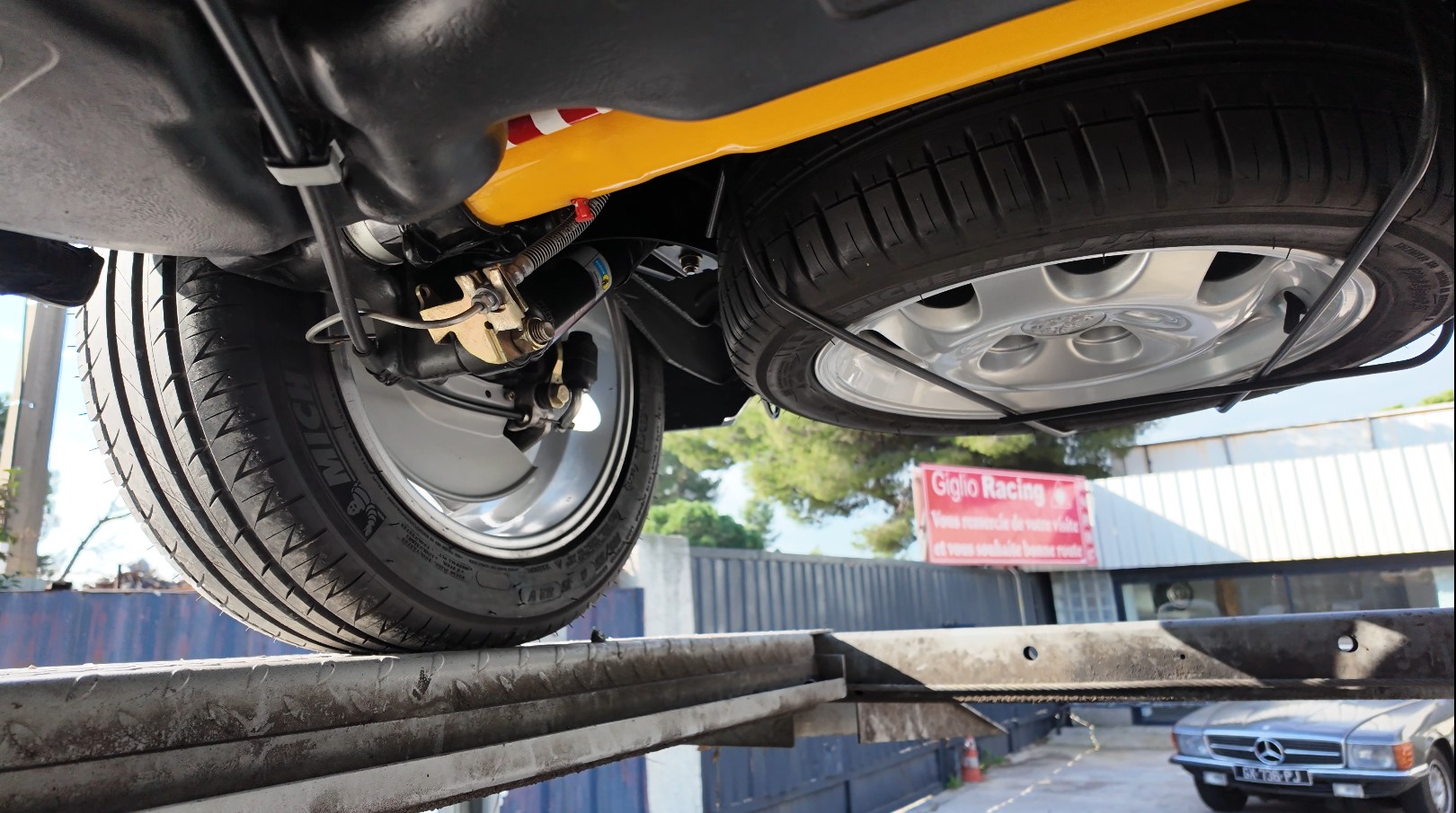 Châssis d'une youngtimer jaune vue de dessous sur pont élévateur, trains roulants et amortisseur visibles