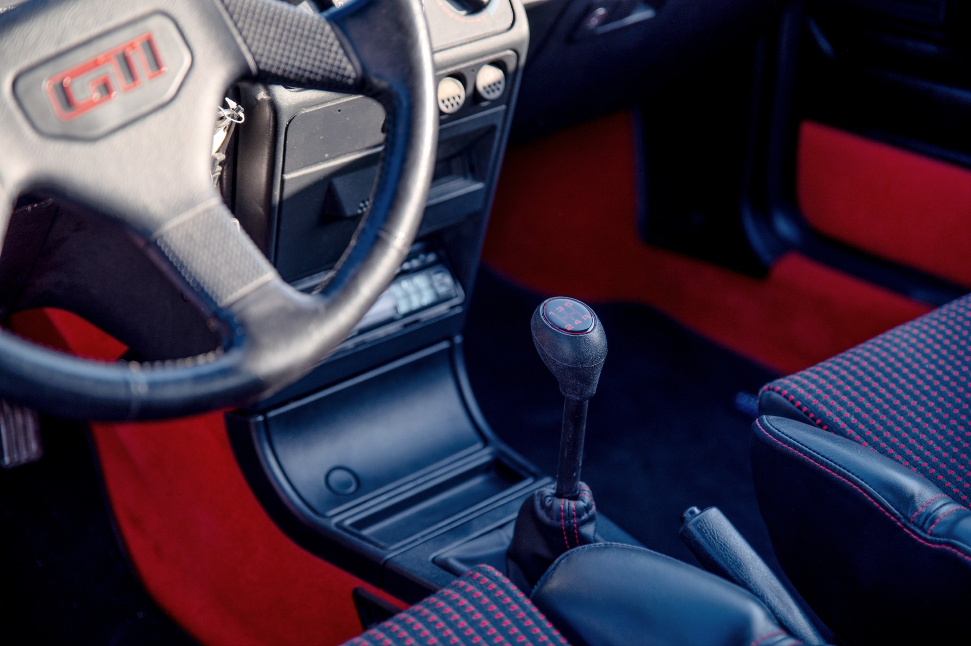 Tableau de bord et levier de vitesse d'une Peugeot 205 GTI avec volant GTI et moquette rouge