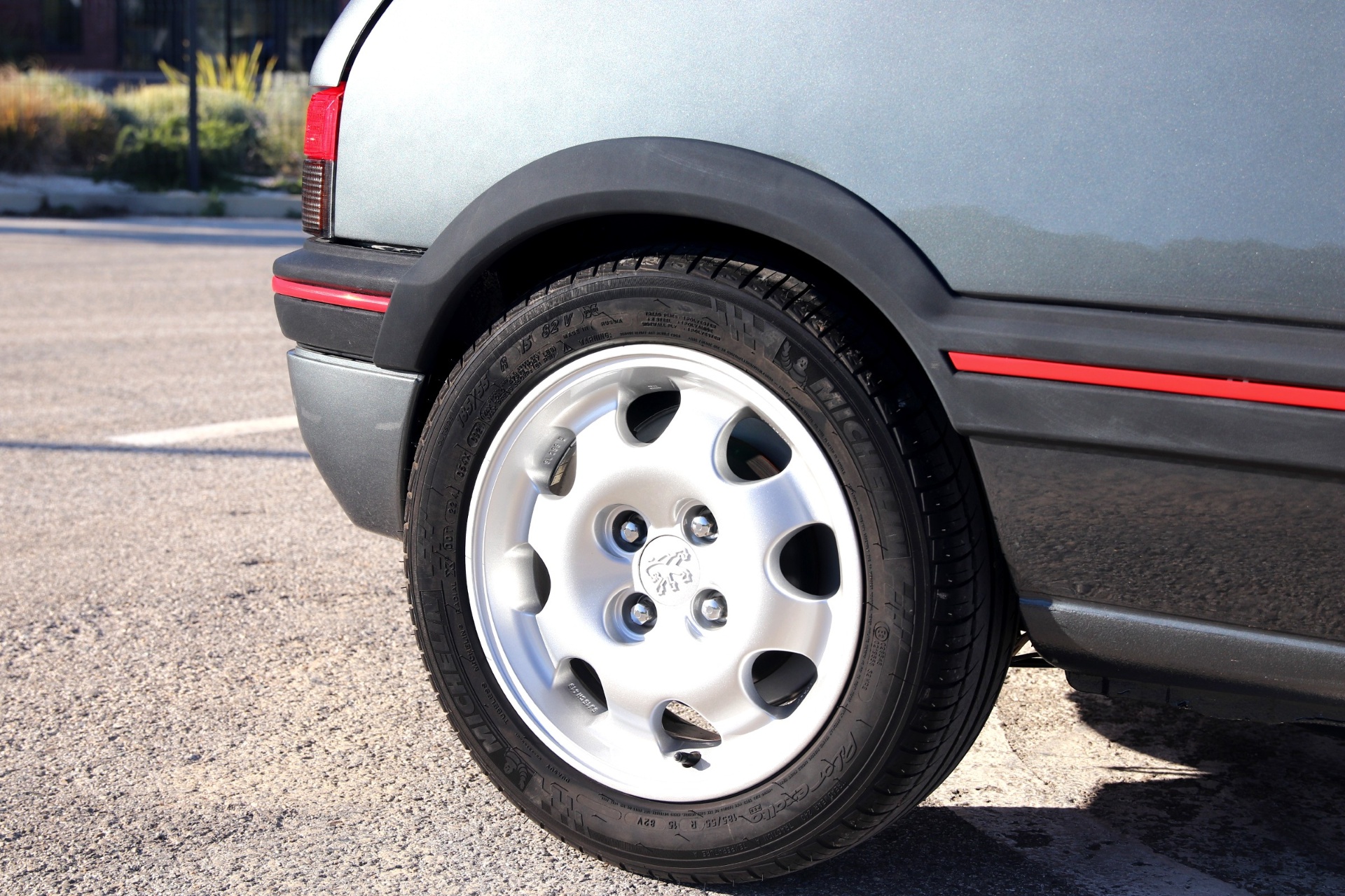 Jante alliage Peugeot Speedline blanche et pneu Michelin sur une 205 GTI grise vue de trois quarts arrière