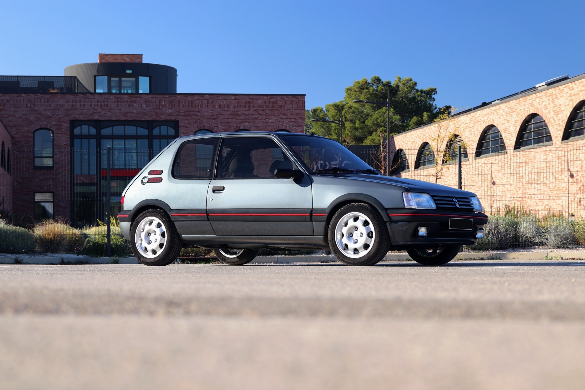 Peugeot 205 GTI 1.9 gris graphite profil complet sur parking ensoleillé