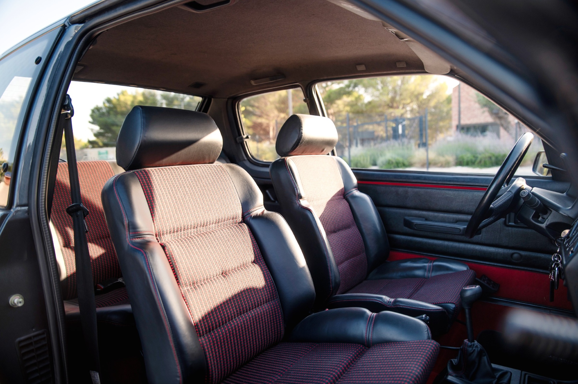 Intérieur Peugeot 205 GTI avec sièges en tissu Quartet rouge et noir, vue côté passager portière ouverte