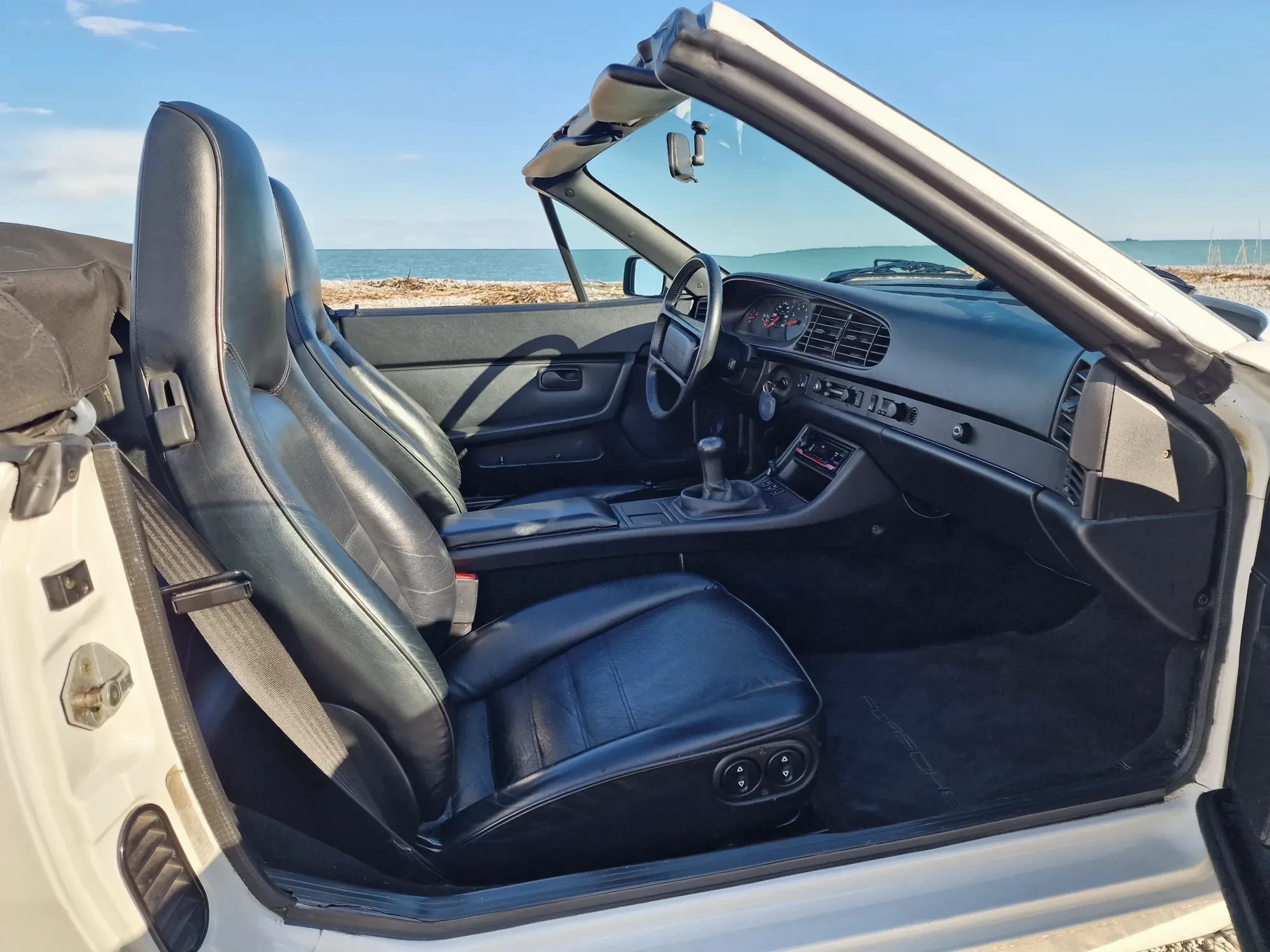 Intérieur cuir noir Porsche 944 cabriolet, sièges baquets et arceau face à la mer