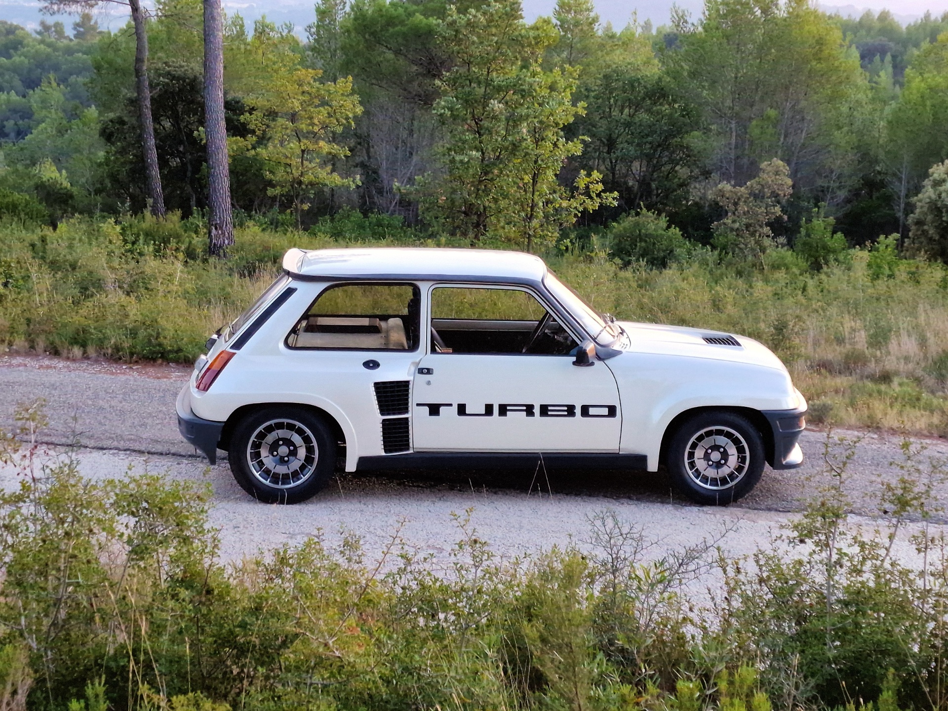 Renault 5 Turbo blanche vue de profil dans un paysage de garrigue